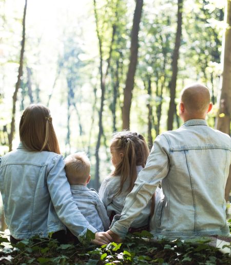 man and woman holding hands together with boy and girl looking at green trees during day