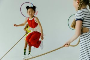 Two young girls enjoy skipping rope indoors, showcasing youth and fun.